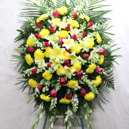 Standing funeral spray with yellow lilies, pink roses, and white blooms