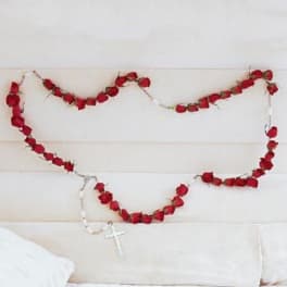 Red rose garland draped across a white upholstered headboard with a rosary hanging below