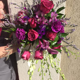 Handheld bouquet of pink roses and purple flowers with trailing white blooms