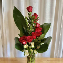 Tall red rose arrangement in a clear glass vase with broad green leaves