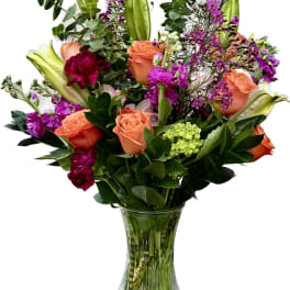 Bouquet of orange roses, purple flowers, and lilies in a glass vase