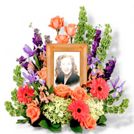 Framed portrait surrounded by orange roses, purple flowers, and pink gerbera daisies