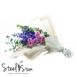 Bouquet of purple orchids and blue flowers wrapped in cream paper