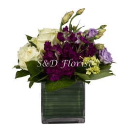 Purple and white floral arrangement in a square glass vase