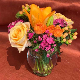 Orange and cream roses with pink filler flowers in a glass vase