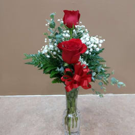 Two red roses in a clear glass vase with baby's breath and a red ribbon