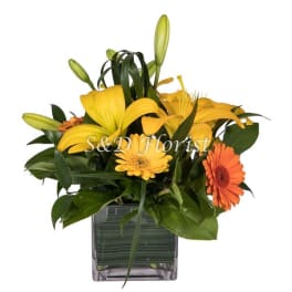 Yellow lilies and orange daisies in a square glass vase