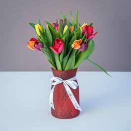 Colorful tulips arranged in a red vase with a white ribbon