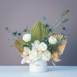 White roses and orchids in a white vase with dried palm fans