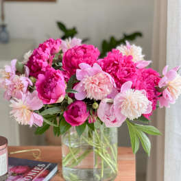 Pink peonies and pale pink flowers arranged in a clear glass vase
