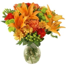 Orange lilies and mixed flowers in a clear glass vase