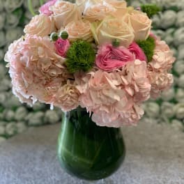 Pink and cream roses with hydrangeas in a green glass vase
