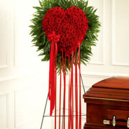 Red heart-shaped floral spray on a stand beside a casket