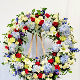 Large floral wreath of red, white, blue, and pale yellow flowers on a wooden stand