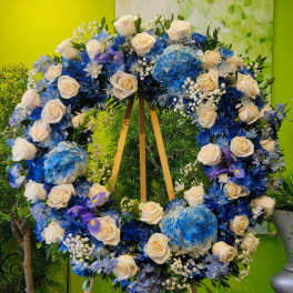 Large heart-shaped floral wreath with white roses and blue flowers on an easel
