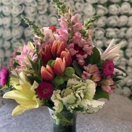 Mixed bouquet of lilies, tulips, and pink flowers in a glass vase