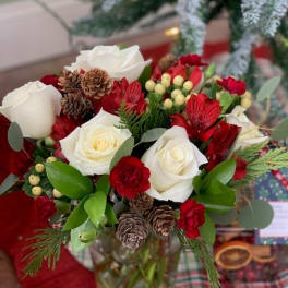 Red and white rose bouquet with pinecones in a glass vase