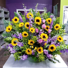 Large arrangement of yellow sunflowers, pink roses, and purple flowers in a green container