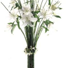 White lilies in a tall glass vase with greenery