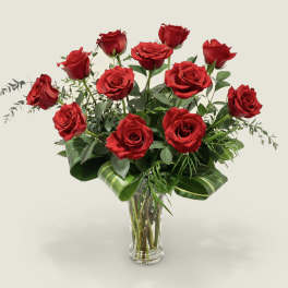 Red roses arranged in a clear glass vase with greenery