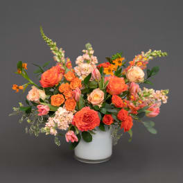 Orange and blush mixed flower arrangement in a white vase