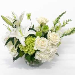 White lilies and roses in a clear glass vase with green accents