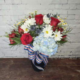 Bouquet of red roses, white daisies, and blue hydrangea in a black vase