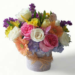 Colorful mixed flower arrangement with roses, gerbera daisies, and hydrangeas in a burlap-wrapped vase