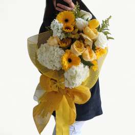 Large hand-tied bouquet of yellow gerberas, white hydrangeas, and roses wrapped in yellow mesh with a bow