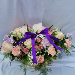 Pastel rose and carnation arrangement with a purple ribbon in a basket