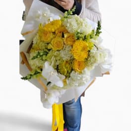 Large hand-tied bouquet of yellow roses, mums, hydrangeas, and white orchids in white wrap