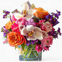Colorful bouquet with roses, orchids, and purple flowers in a glass vase