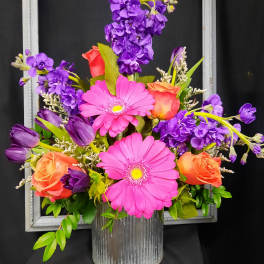 Pink gerbera daisies and orange roses in a silver vase with purple flowers