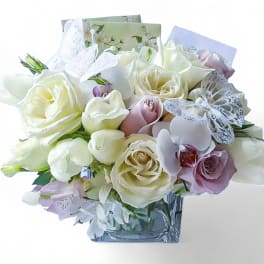 Bouquet of white and blush roses with orchids in a square glass vase