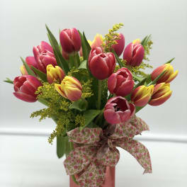 Pink and yellow tulips in a pink vase with a floral ribbon