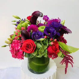 Bright mixed bouquet in a green glass vase with red, pink, purple, and green blooms