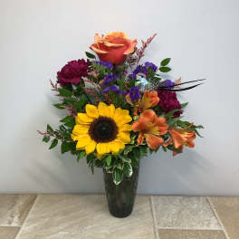 Mixed bouquet with a sunflower, roses, and orange lilies in a dark vase