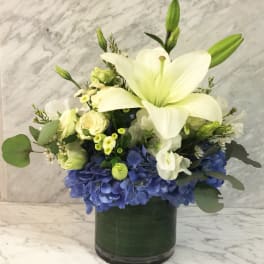White lily and blue hydrangea arrangement in a dark glass vase