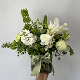 White floral arrangement in a glass vase with a green ribbon