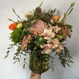 Loose peach and orange mixed flower arrangement with green accents in a clear glass vase
