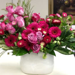 Pink roses and magenta daisies arranged in a white vase