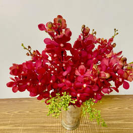Red orchid arrangement in a clear glass vase with green berry accents