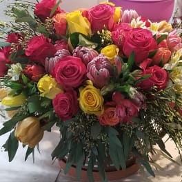 Mixed bouquet of pink and yellow roses with assorted blooms in a round container