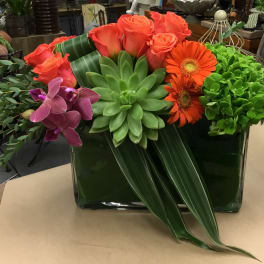 Succulent and rose arrangement with orange gerbera daisies in a glass vase