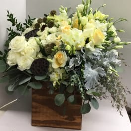 White and pale yellow floral arrangement in a wooden box with greenery
