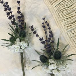 Two small lavender and white floral boutonnieres with pearl pins