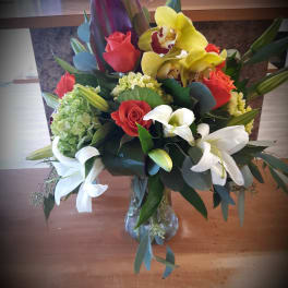 Mixed bouquet with roses, orchids, lilies, and hydrangea in a glass vase