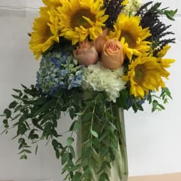 Sunflower and rose arrangement in a clear vase with trailing greenery