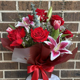 Bouquet of red roses and pink lilies in burgundy wrap with a red ribbon