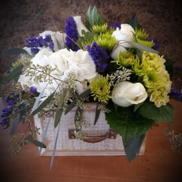 Bouquet of white roses, green chrysanthemums, and purple filler flowers in a wooden box